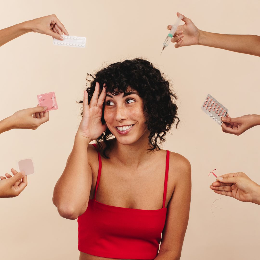 weiblich gelesene person mittig bekommt von der seite von sechs händen verschiedene verhütungsmittel gereicht, person hält sich hand seitlich schützend vor die augen