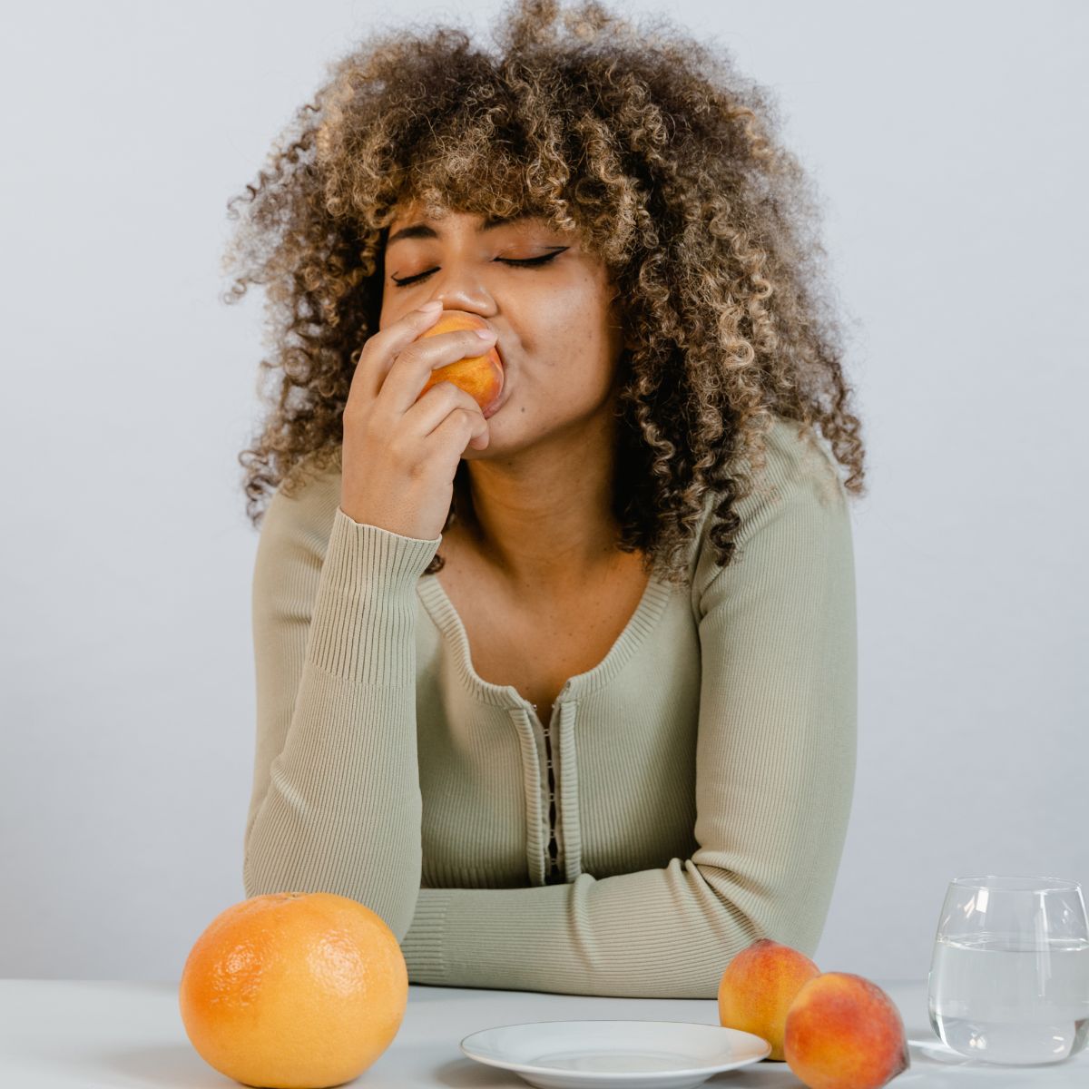 weiblich gelesene Person beißt in einen Pfirsich, gesunde ernährung für die haare, ernährung bei haarausfall
