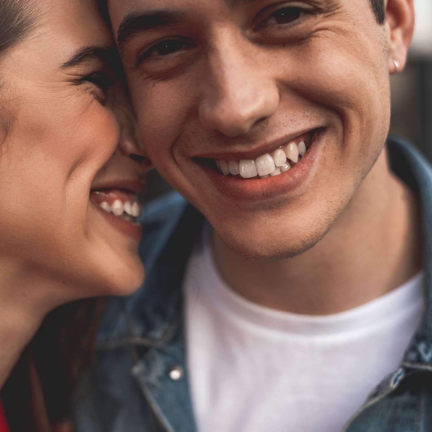 Porträt einer weibich gelesenen und einer männlich gelesenen Person, männliche Person schaut in Kamera, weibliche Person lehnt ihre Nase an männliche Person