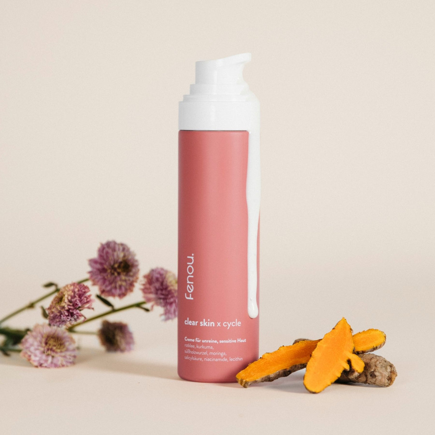 Eine Flasche clear skin Creme, daneben Kurkuma und pastellfarbenen Blumen