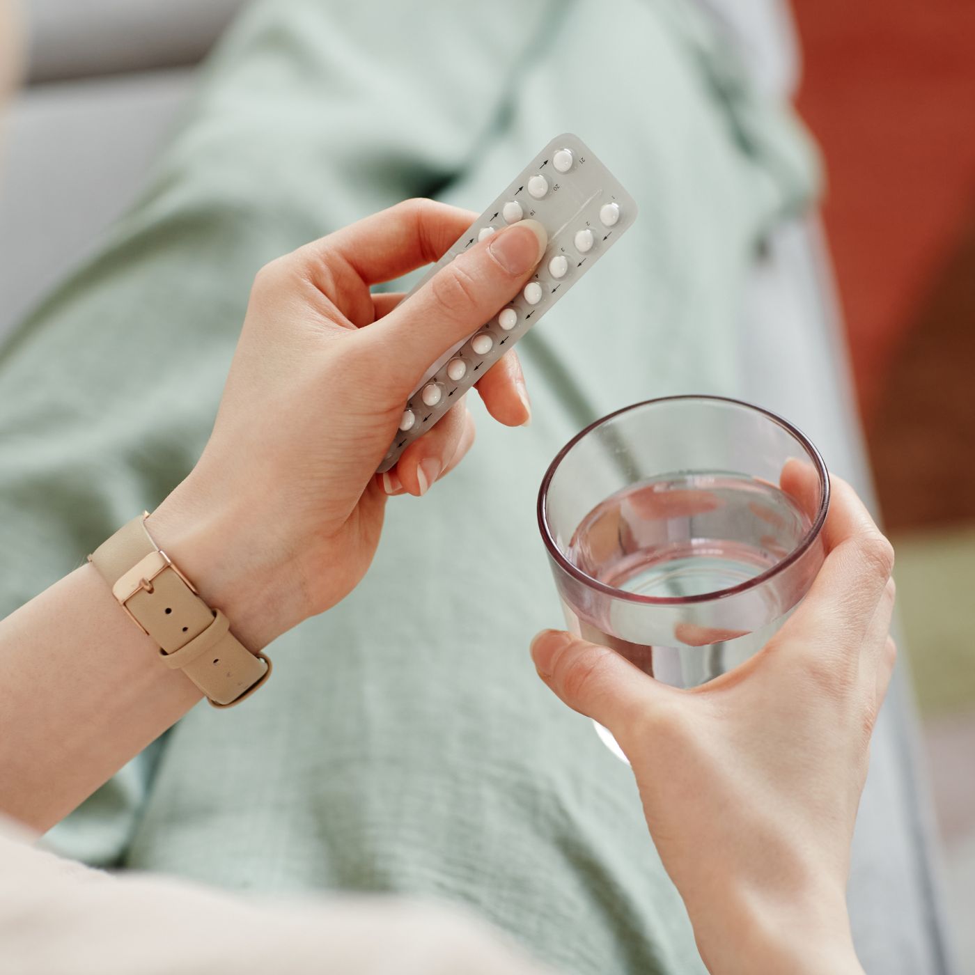 Person von oben fotografiert hält eine Packung Antibabypille und ein Wasserglas in der Hand