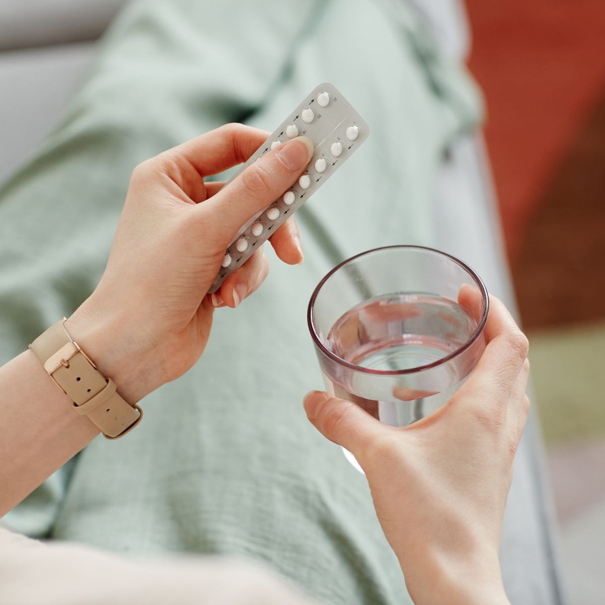 Person von oben fotografiert hält eine Packung Antibabypille und ein Wasserglas in der Hand