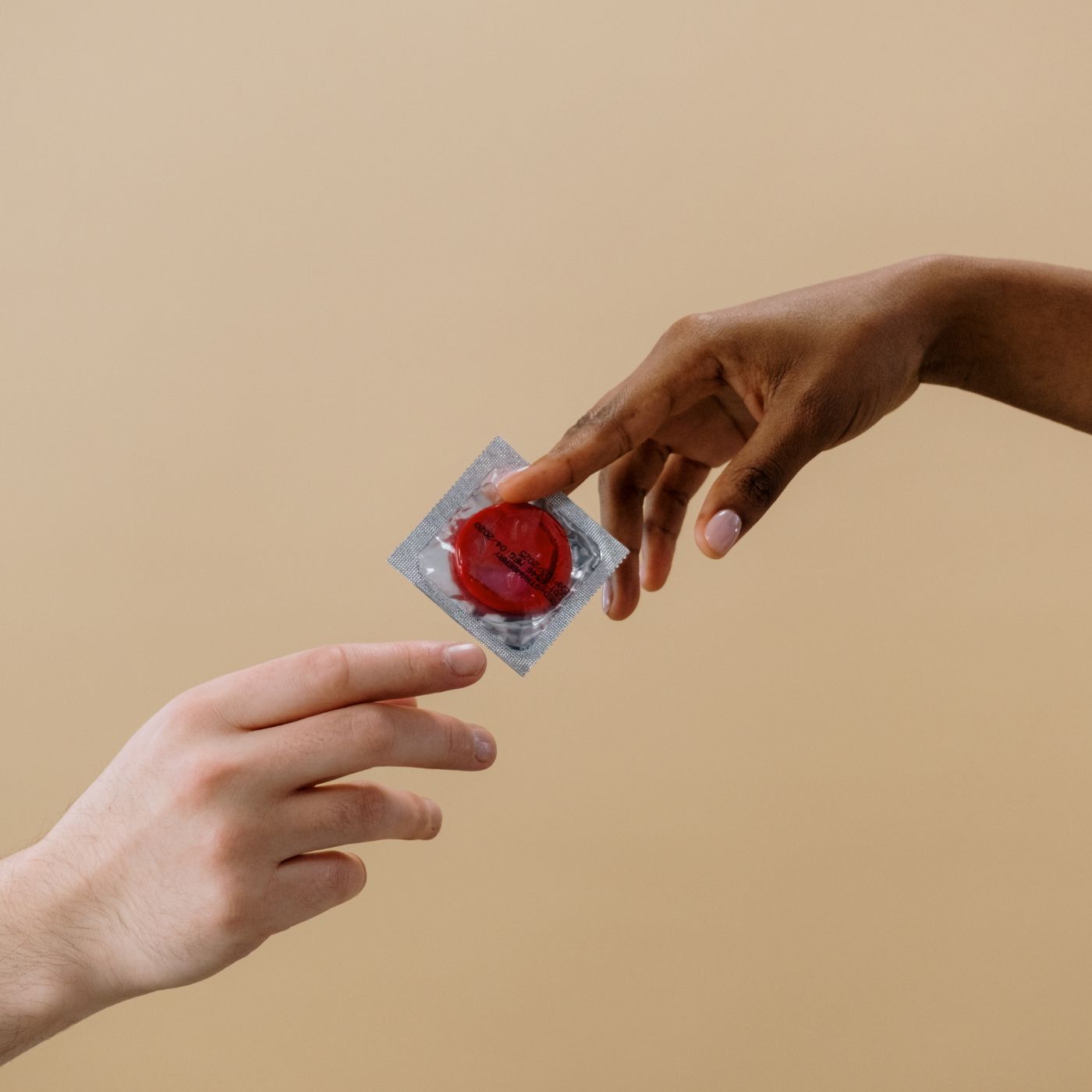 weiblich gelesene hand reicht männlich gelesener hand ein rotes kondom in verpackung