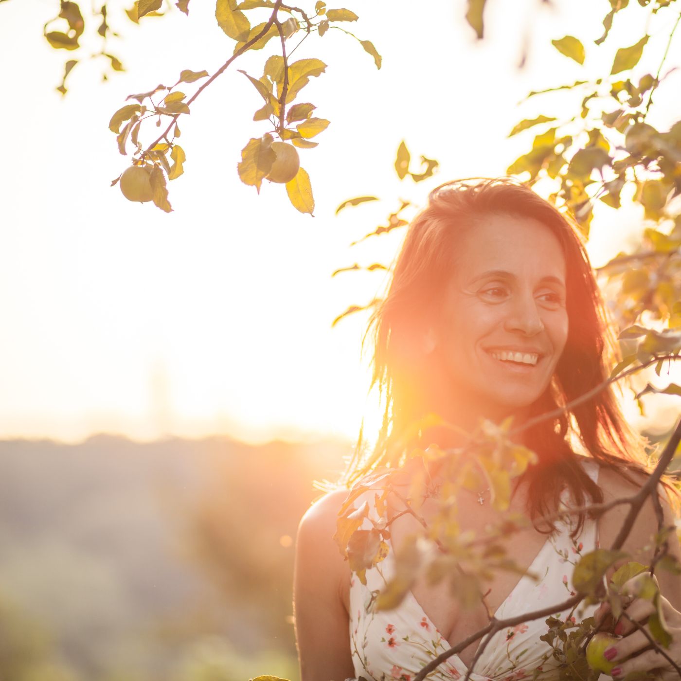 weiblich gelesene person steht lachend hinter einem zweig im sonnenuntergang