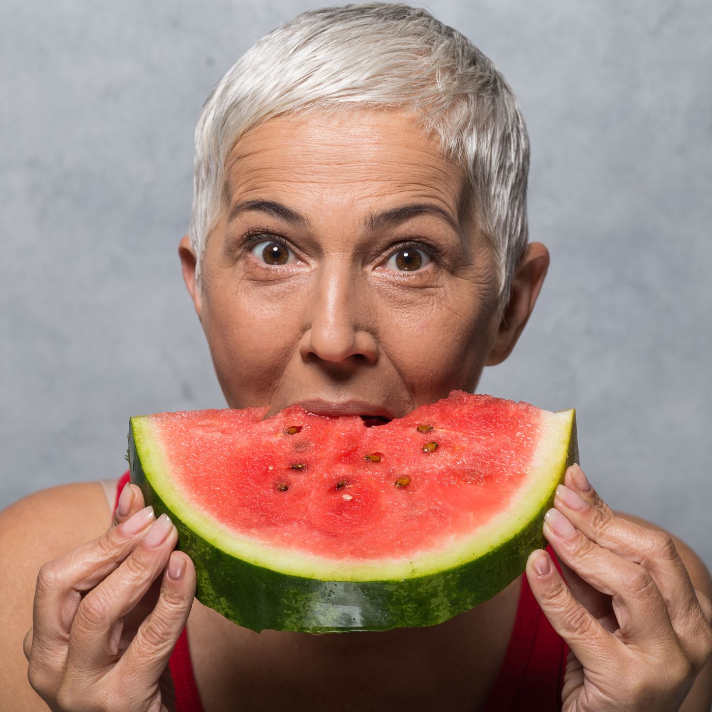 weiblich gelesene Person mit kurzen, silbernen Haaren hält eine Scheibe Melone vor ihren Mund