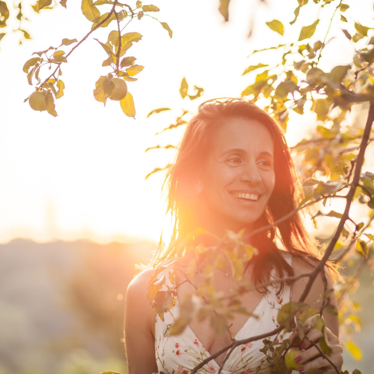 weiblich gelesene person steht lachend hinter einem zweig im sonnenuntergang