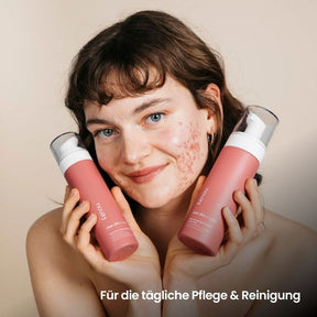 weiblich gelesene Person mit Gesichts-Akne hält fenou clear skin Creme und Reinigungsschaum neben ihr Gesicht